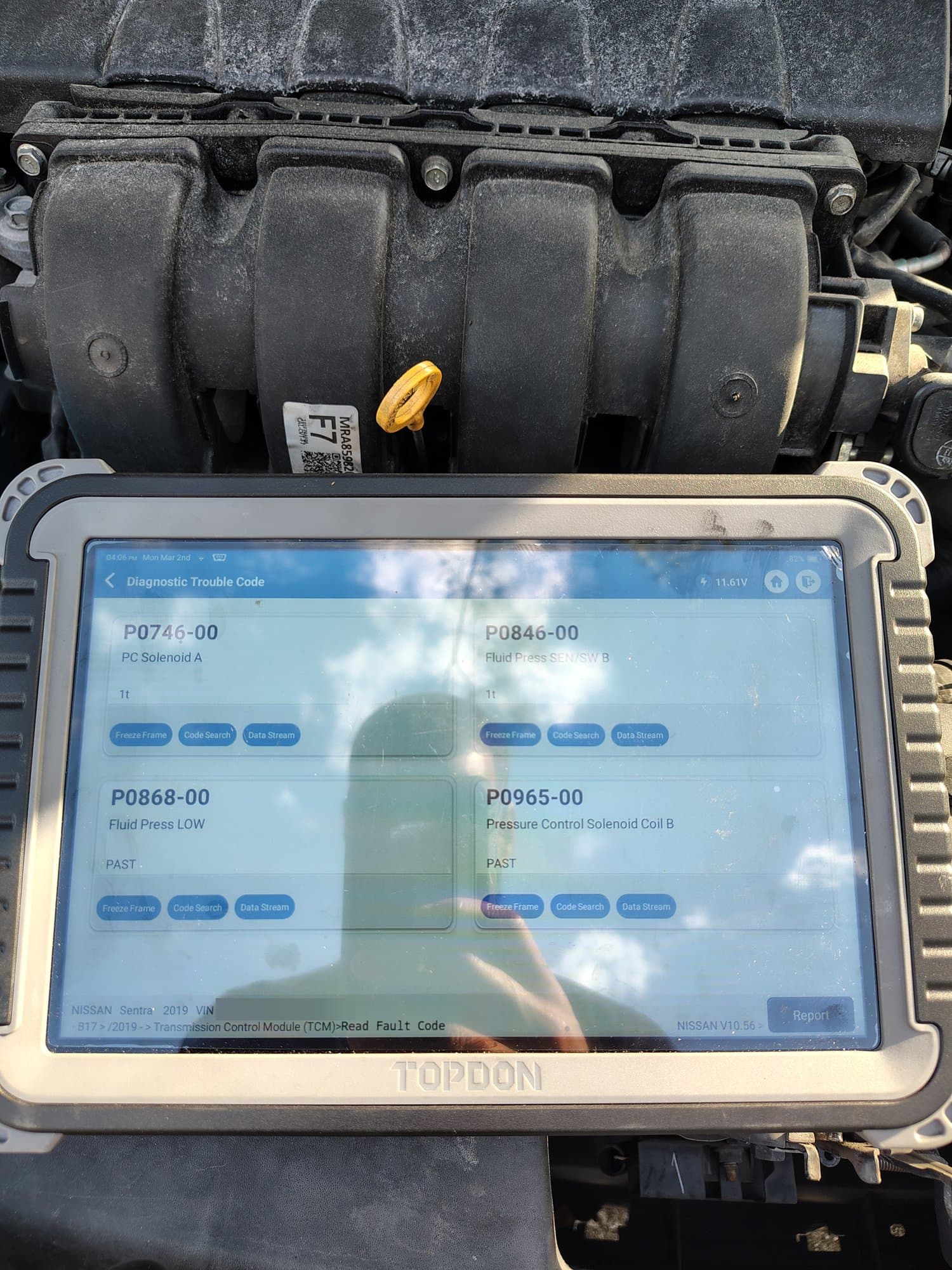 A diagnostic scanner tablet resting on an engine, its screen showing four transmission fault codes pulled from the car's control module
